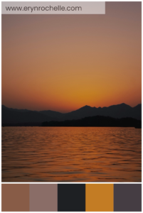 Silhouette of a mountain near a calm sea during sunset, featuring warm brown, soft mauve, deep charcoal, vibrant amber, and muted plum tones in a tranquil natural setting.
